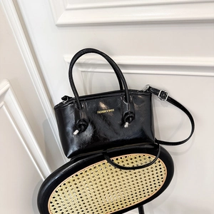 Glossy black wax leather tote bag with gold lettering shown on a textured chair