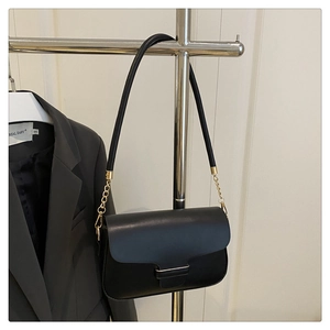 Detail of a black leather shoulder bag with gold metal buckle on a grey blazer