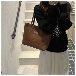 Detailed view of brown leather tote bag with gold bow emblem and metal rivets