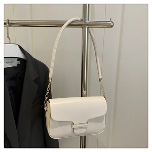 Detail view of cream-colored shoulder bag with gold chain strap on grey blazer