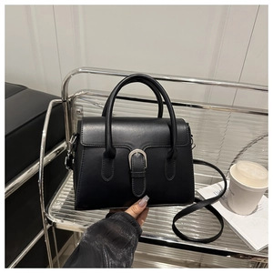 Detail of black faux leather handbag featuring silver horseshoe buckle and adjustable strap