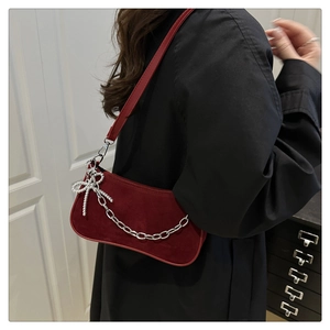 Detail of burgundy frosted leather shoulder bag with silver chain and bow charm on model