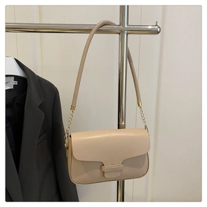 Detail of beige shoulder bag with gold clasp and chain strap hanging by a grey blazer