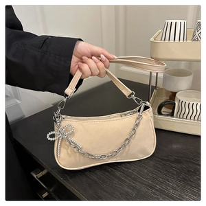 Detail of apricot hobo bag featuring silver chain strap and beaded bow charm accessory