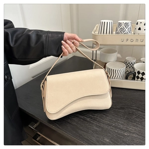 Close-up of beige underarm bag with asymmetric flap and smooth matte texture finish