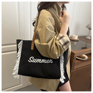 Détail d'un sac cabas en toile noire avec broderie Summer blanche et franges latérales