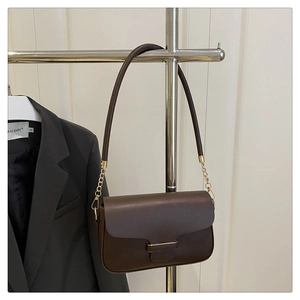 Detail of dark brown leather handbag featuring golden metal bar and elegant strap chains