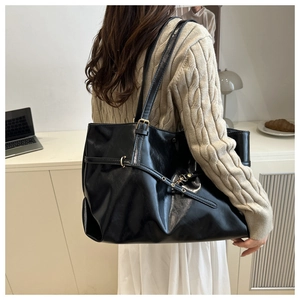 Detail of black large tote bag with glossy leather texture and gold hardware on shoulder