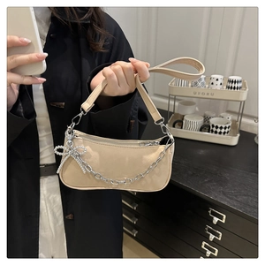 Detail of apricot baguette bag with silver chain and bow charm on a leather strap
