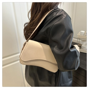 Minimalist beige underarm bag with asymmetrical flap worn over a black leather jacket