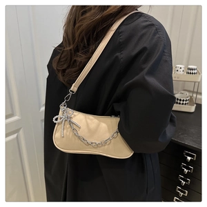 Detail of beige faux leather hobo bag featuring silver chain and pearl bow charm accessory