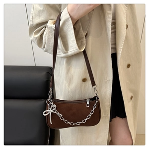 Close-up of brown suede shoulder bag with silver chain and rhinestone bow on a model