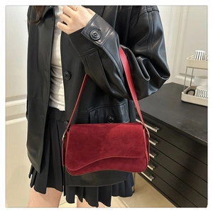 Deep red suede underarm bag with asymmetric wave flap shown styled on a model