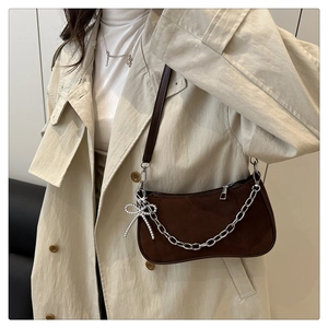 Brown matte suede shoulder bag with silver chain and bow charm shown on model in a trench coat