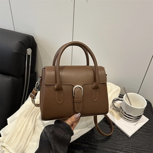 Brown leather crossbody bag with silver buckle and top handle in a lifestyle setting
