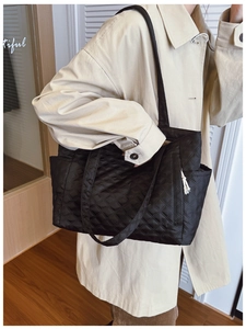 Close-up of a large black quilted tote bag showing side pockets and premium texture