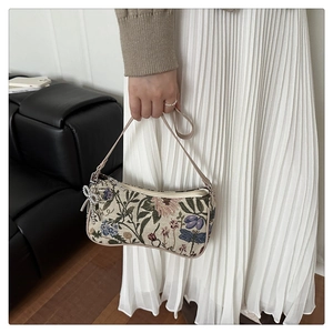 Detail of floral embroidery on a vintage baguette bag with bow pendant and zipper