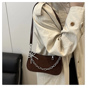 Detail of matte brown hobo bag featuring a silver chain and delicate bow charm accent