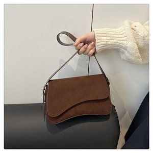Close-up of a dark brown suede shoulder bag with a unique wavy asymmetrical flap design