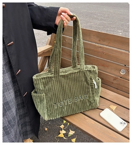 Detail der grünen Cord-Einkaufstasche mit TOTE BAG-Stickerei auf einer Holzbank