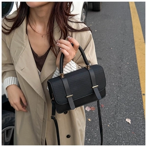 Detail of black crossbody bag with twill texture and gold hardware on beige coat