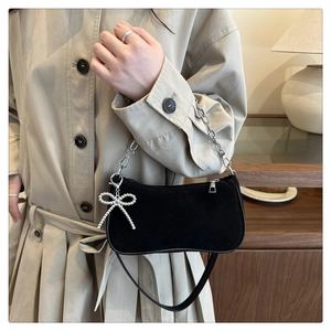 Close-up of black suede underarm bag featuring silver chain and beaded bow pendant charm