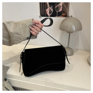 Close-up of black velvet shoulder bag with irregular curved flap and gold hardware