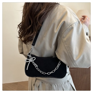 Detail of black suede hobo bag with silver chain and bead bow charm on a shoulder strap