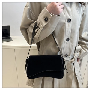 Detail of black suede shoulder bag with wavy edge worn with a beige trench coat