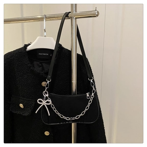 Detail of black suede underarm bag with silver chain and pearl bow charm accessory