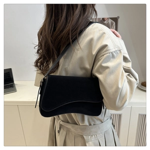 Minimalist black suede underarm bag with wavy flap shown on a trench coat model