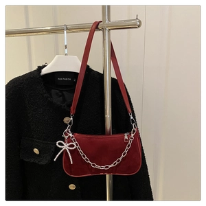 Detail of red velvet handbag featuring silver chain and pearl bow charm accessory