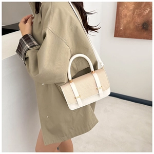 Detail of a white leather and beige woven crossbody bag worn with a green trench coat