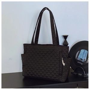 Detailed view of black quilted tote bag featuring diamond pattern and functional side pockets