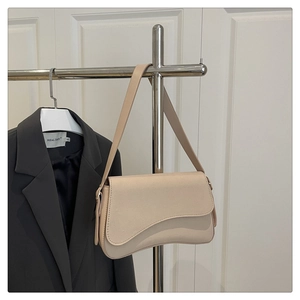 Detailed close-up of a minimalist beige underarm bag featuring a curved flap and suede texture