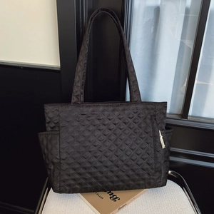 Black quilted tote bag with large capacity and shoulder straps on a white chair