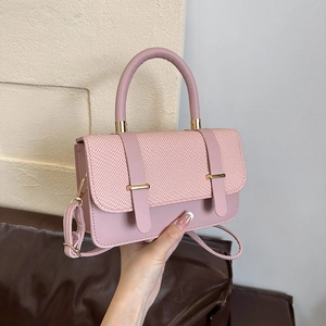 Pink patchwork messenger bag with woven texture and gold accents held by hand