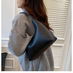 Model wearing a minimalist black leather underarm bag with an embossed logo
