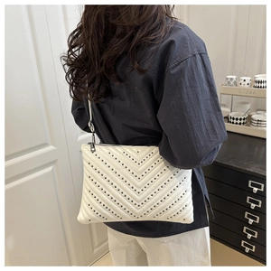 Detail view of a white leather crossbody bag featuring V-shaped quilting and black rivets