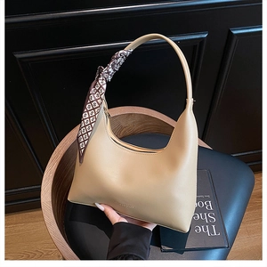 Detail of beige hobo bag with fashion logo and decorative silk scarf on the handle