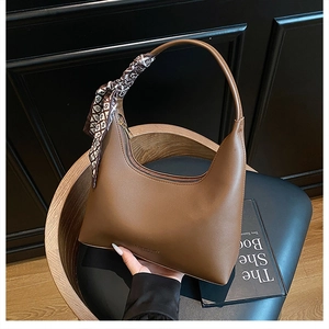 Close-up of brown crescent hobo bag with printed silk scarf detail on handle