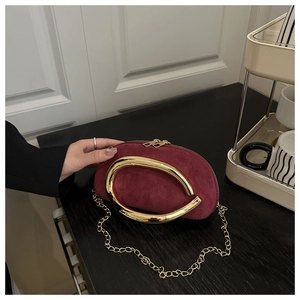 Detail of burgundy suede evening clutch with a thick gold C-shaped metal handle