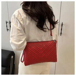 Close-up of red quilted leather envelope bag with metal rivets and silver zipper details