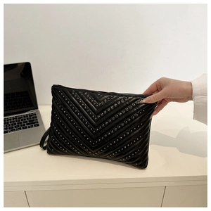 Close-up of black leather clutch bag with V-quilted texture and metal stud details