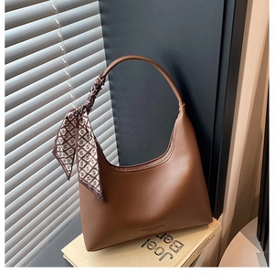 Detailed view of brown leather crescent bag with patterned silk scarf on handle