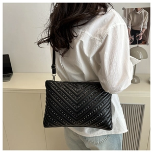 Detail of black quilted leather crossbody bag with silver rivet V-pattern on model