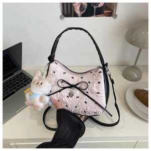 Détail du sac bandoulière rose gaufré avec nœud noir et breloque lapin en peluche blanc