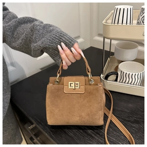Detail showing brown suede and leather crossbody bag with a gold metal turn-lock buckle