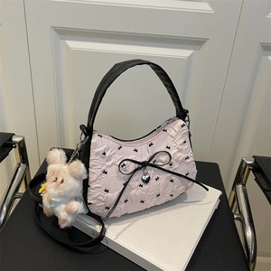 Sac sous le bras rose gaufré avec nœuds noirs et breloque lapin sur un banc en cuir