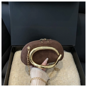 Detail of a dark brown suede clutch with gold C-handle and chain in a gift box